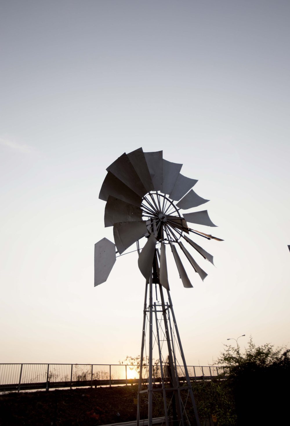 A steel windpomp against a pale sky, the sun setting behind it.